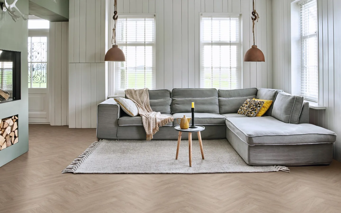 Woonkamer in landelijke stijl met visgraat vloer, gemoedelijke hoekbank en kachel.