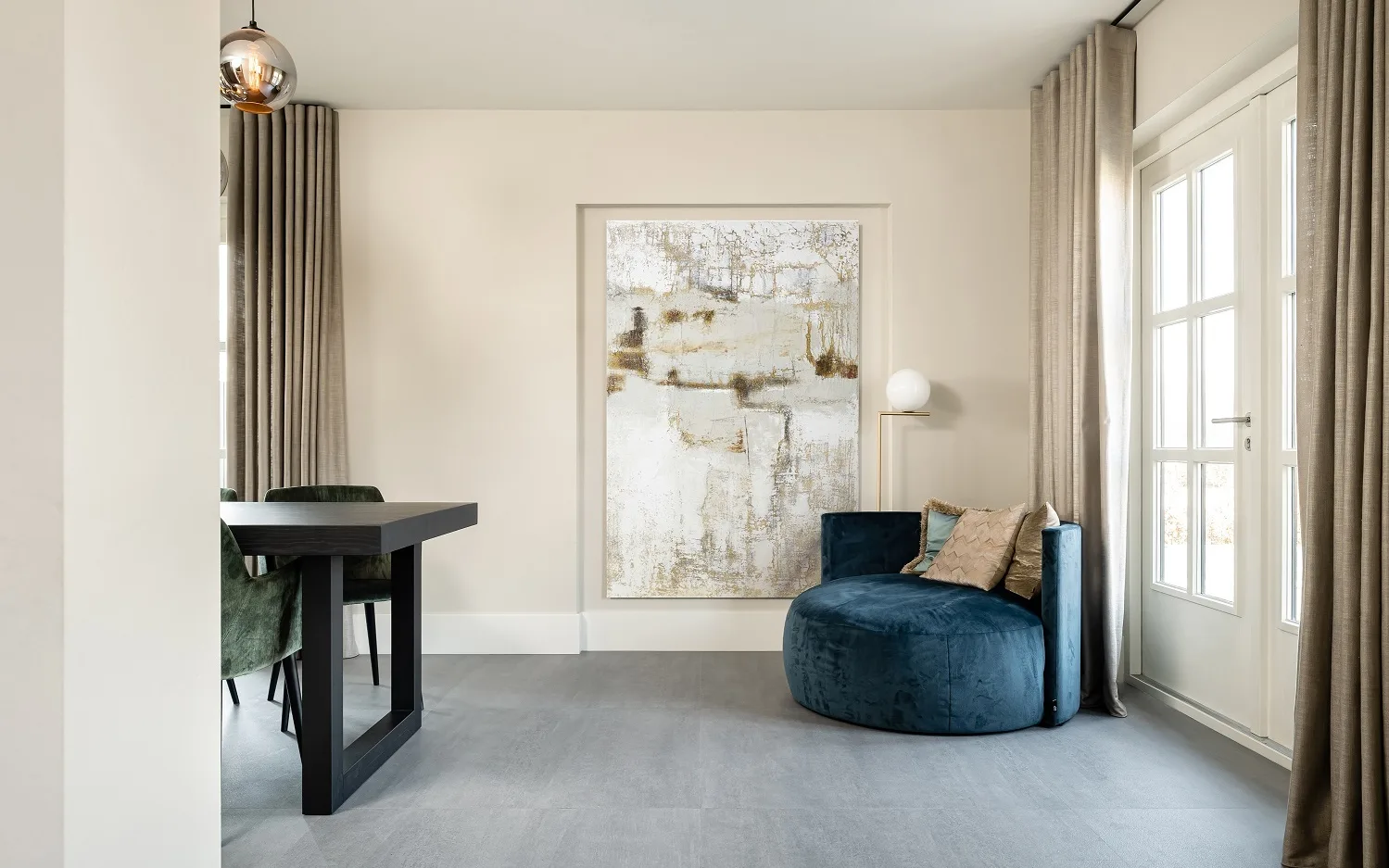 Woonkamer met beton look vinylvloer in grijs, gordijnen in een warme bruintint en een prachtig schilderij.