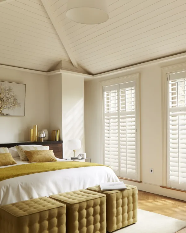 Hotel chique stijl slaapkamer met 2persoons bed in beige en oker tinten en grote ramen met witte shutters