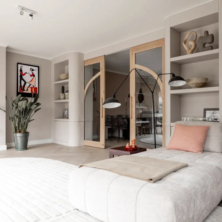 Zonnige woonkamer met gebogen houten deuren met glas en Art Nouveau boekenkasten in natuurlijke kleuren.