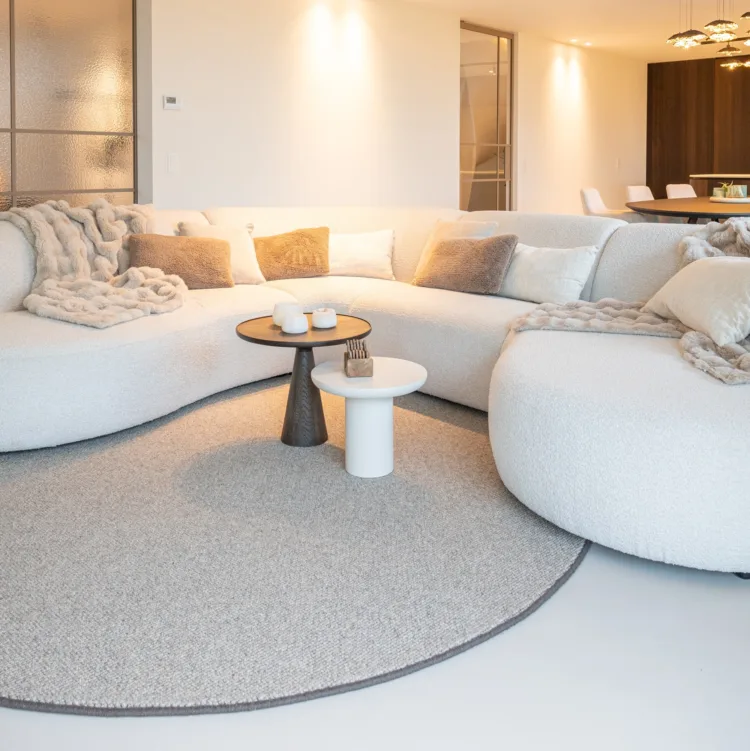 Woonkamer met bronzen stalen deuren, kast op maat, ovale bank en beige vloerkleed